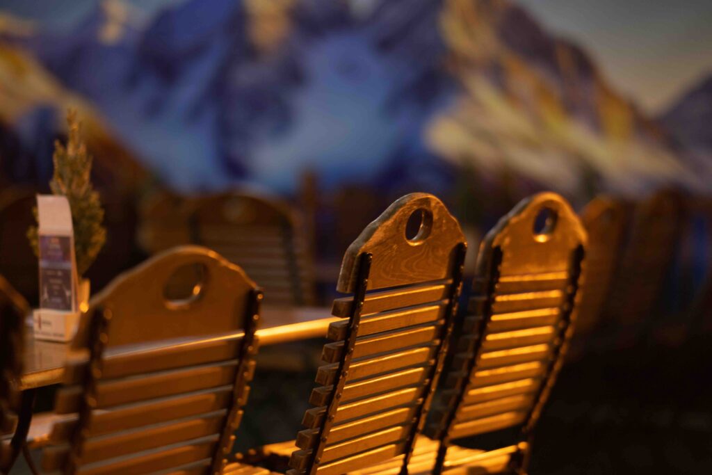 Holzstühle und gedeckte Tische in der Almhütte im anona Icedome Leipzig mit Alpenkulisse im Hintergrund
